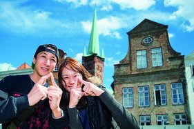 Die Japanische Touristen Jun und Kayako zeigen das Sieben-Türme-Symbol mit ihren Zeigefingern - vor dem St. Petri Turm