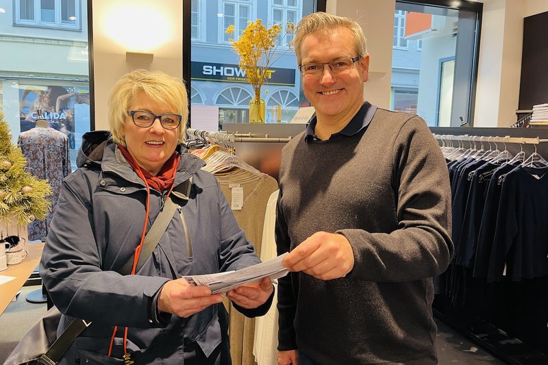Frau Kempke hält die Verlosungskarten im Geschäft „Bettenhaus Struve“, Herr Ginap zieht daraus den Gewinner.
