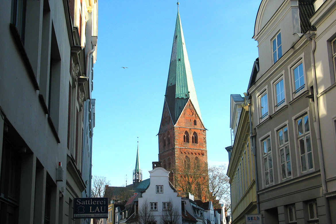 Kirchturm St.-Aegidien-Kirche ragt über die historischen Altstadtdächer Lübecks empor. Der Himmel ist ohne Wolken. 