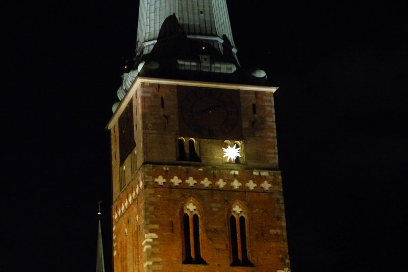 Ein leuchtender Weihnachtsstern ist unterhalb der Uhr von St. Jakobi zu sehen. Es ist Nacht.