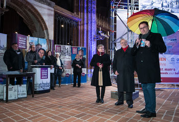 Pröpstin Petra Kallies, Herr Böhning und Bürgermeister Jan Lindenau (mit einem aufgespannten regenbogenfarbenen Regenschirm) stehen nebeneinander in der St.-Marien-Kirche - Copyright: Ev.-Luth. Kirchenkreis Lübeck-Lauenburg