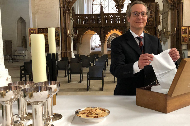 Heiko Gruhl bereitet den Altar für einen Gottesdienst mit Abendmahl vor. Zu sehen sind Oblaten und Kelche für den Wein.