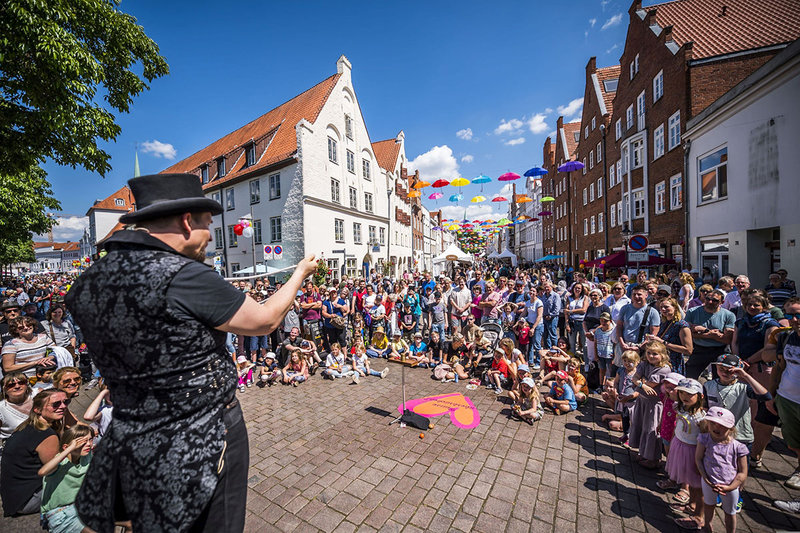 Roland Henning vom Zaubertheater Lübeck zeigte seine Zauberkunst. Er steht im Vordergrund in schwarzer Kleidung und schwarzem Hut, vor ihm stehen und sitzen eine vielzahl an Besuchern