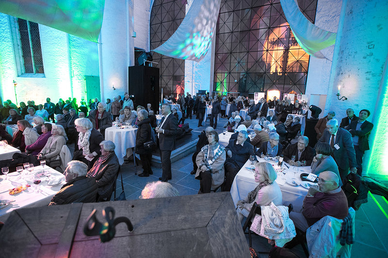an Tischen sitzende und stehende Fest-Versammlung im Dom mit blau-grüner Beleuchtung