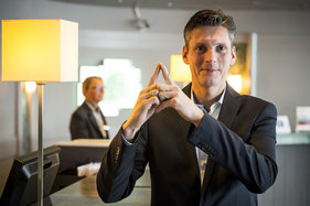 Frank Senger Generalmanager vom Holiday Inn macht das Sieben-Türme-Symbol mit seinen Zeigefingern. Die Finger zeigen eine Turmspitze.